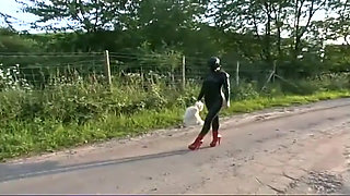 Fetish slave in latex walks and sucks a dildo on the grass